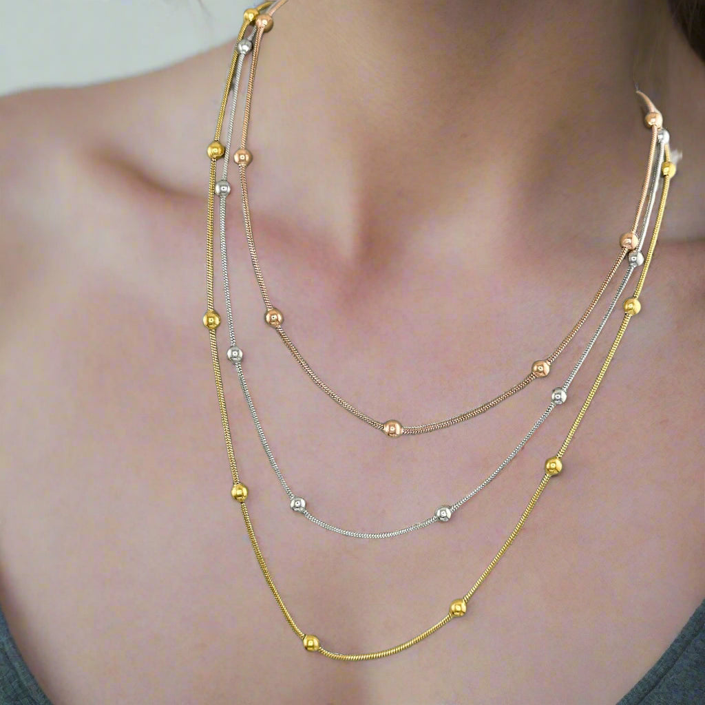 Tri-colour layered necklace set displayed on a grey jewellery bust, featuring gold, silver, and rose gold beaded stainless steel chains with 18K gold PVD plating.
