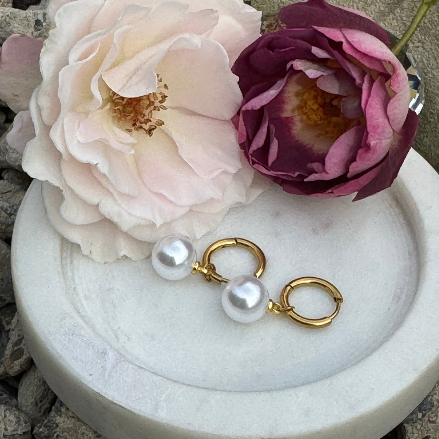 Pearl earrings laying on a white plate with stunning white and purple roses