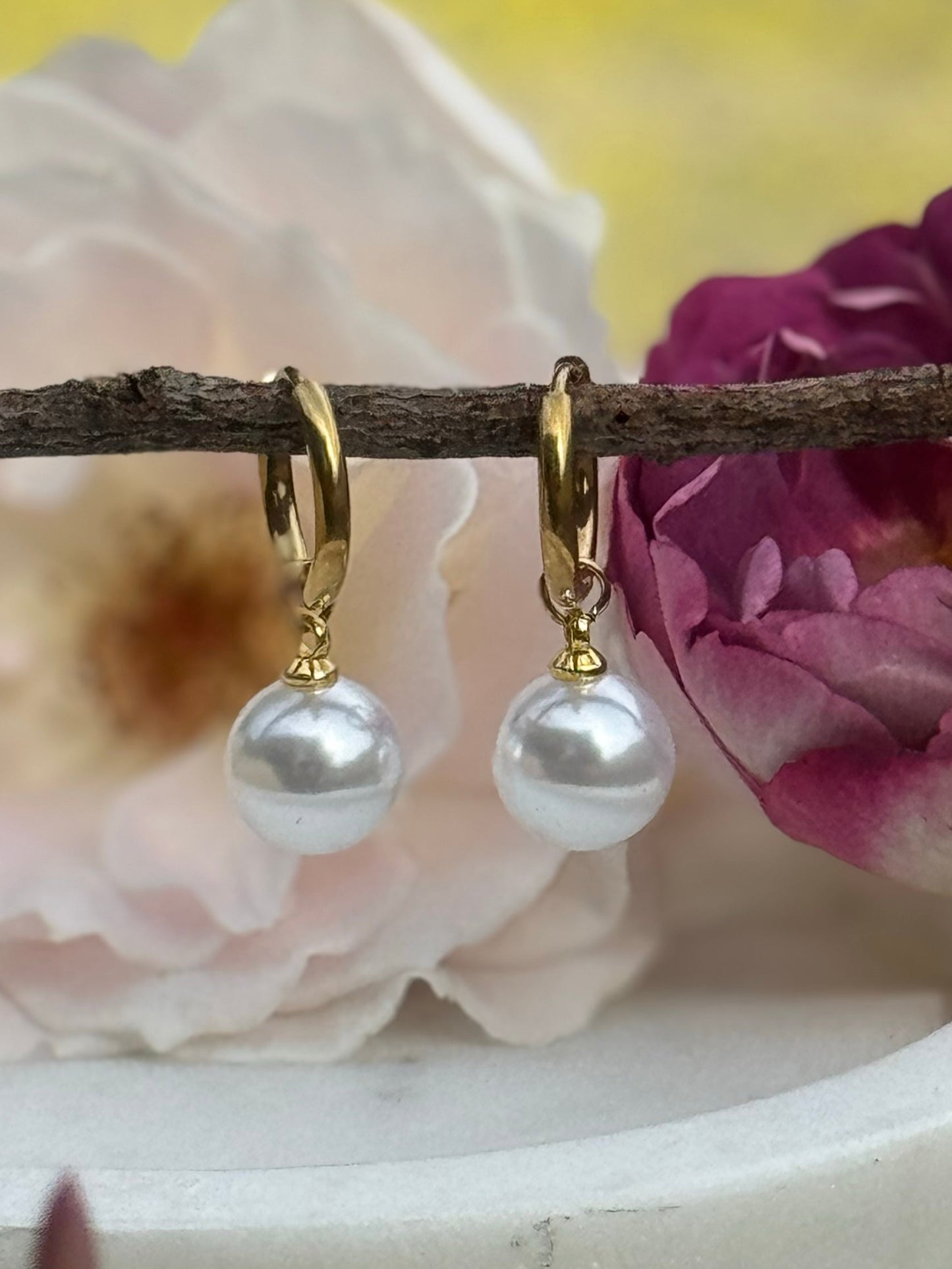 pearl drop earrings hanging on a branch for display with roses in the background