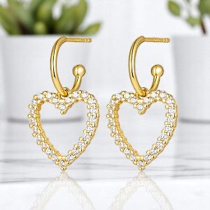 Gold heart-shaped dangle earrings with rhinestones, made of 925 sterling silver, displayed on a marble surface with plants in the background.